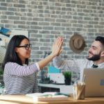 Two happy coworkers high five in work place